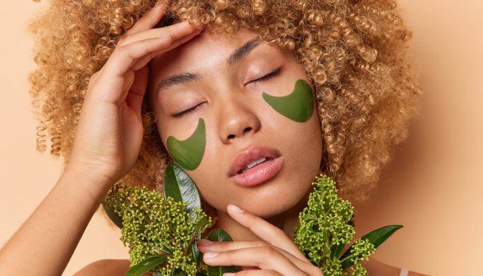 Close up portrait of woman with under eye patches and greenery. 
