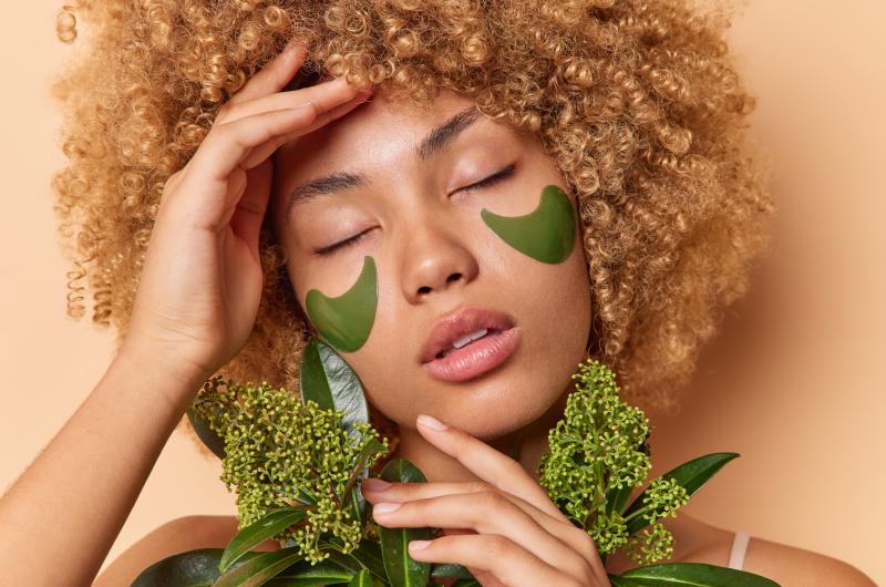 Close up portrait of woman with under eye patches and greenery. 
