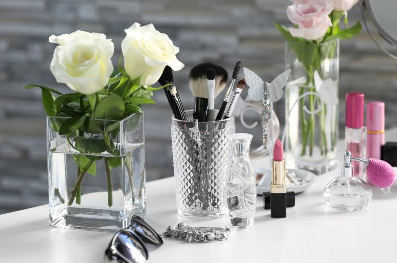 A collection of cosmetics arranged on a white vanity table with glass jars and roses.